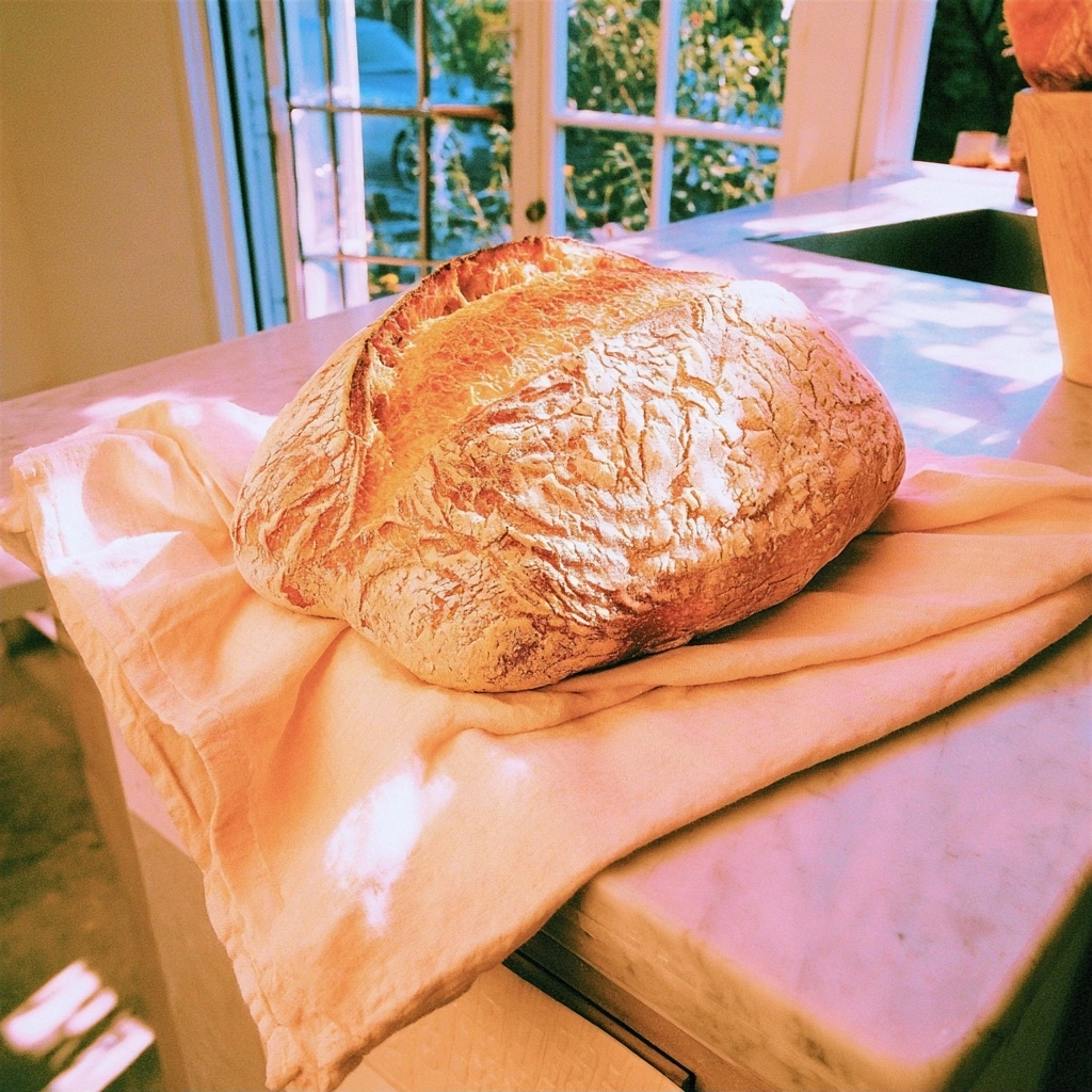 A freshly baked loaf of crusty bread resting on a white cloth in a sunlit kitchen.