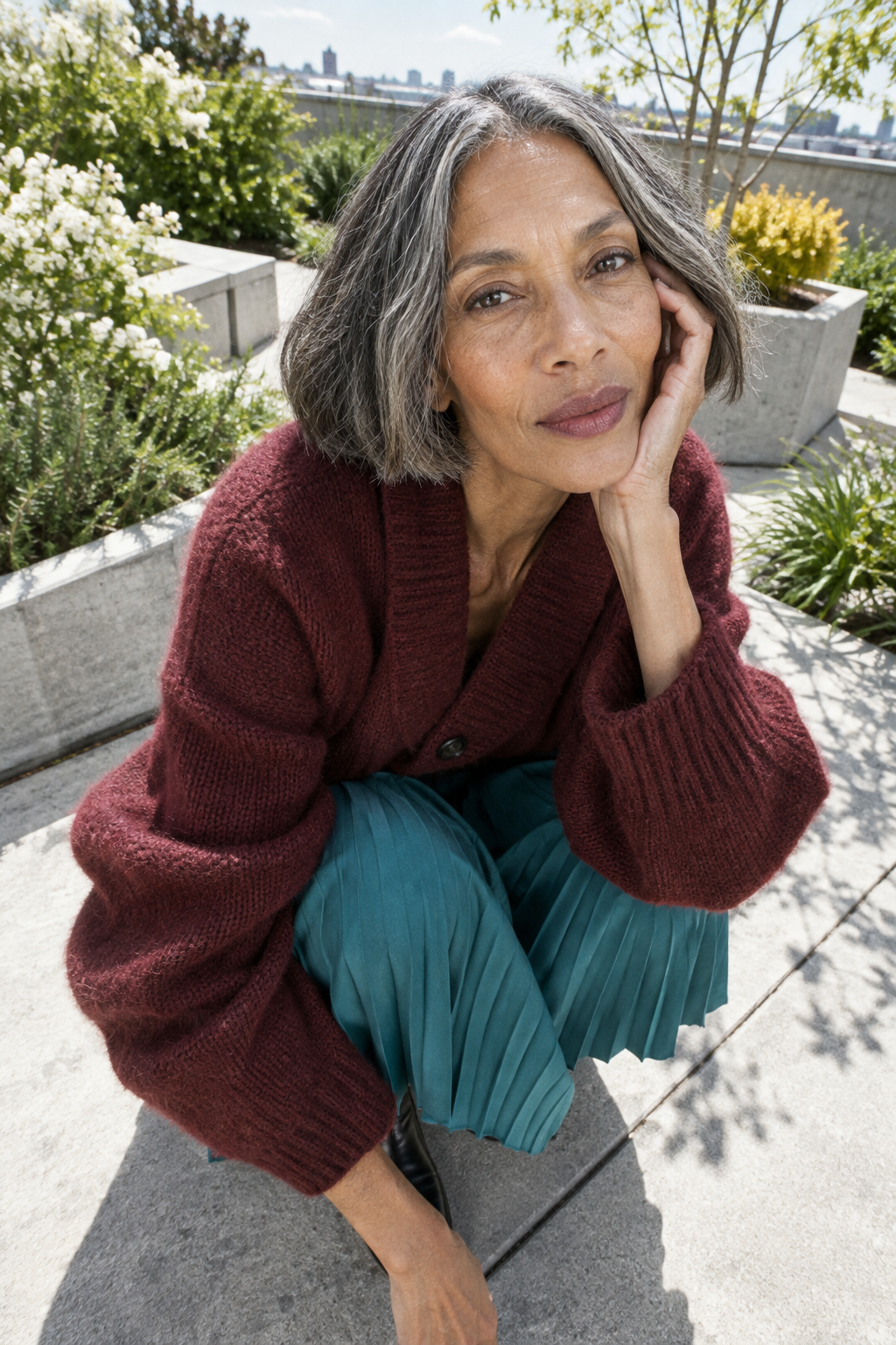 Portrait of a smiling woman with salt and pepper hair wearing a burgundy sweater and teal trousers.